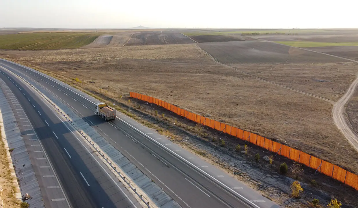 Eskişehir–Konya yolu ve arazinin yol cephesi — yolda ilerleyen bir kamyon ve arazi sınırı boyunca uzanan şantiye paneli